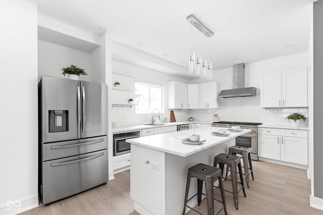 kitchen featuring appliances with stainless steel finishes, backsplash, sink, a center island, and wall chimney range hood