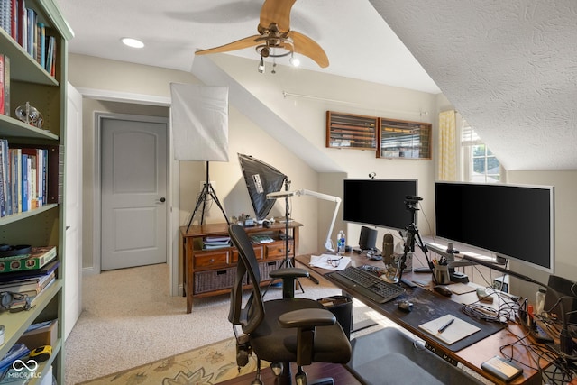 carpeted office space featuring ceiling fan, vaulted ceiling, and a textured ceiling