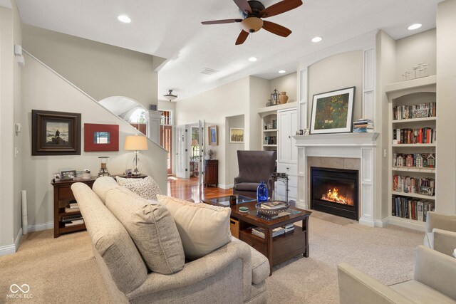 living room with ceiling fan, built in shelves, light carpet, and a fireplace