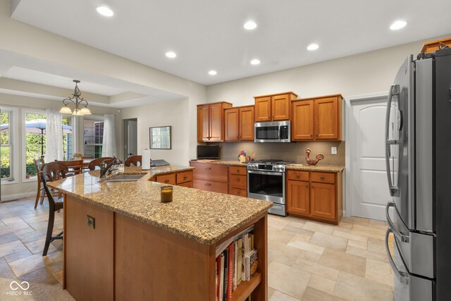 kitchen featuring light stone countertops, appliances with stainless steel finishes, sink, decorative light fixtures, and a center island with sink