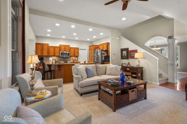 living room featuring ceiling fan, light colored carpet, and ornate columns