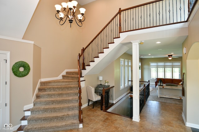 stairway featuring ceiling fan with notable chandelier, tile patterned floors, decorative columns, and a high ceiling