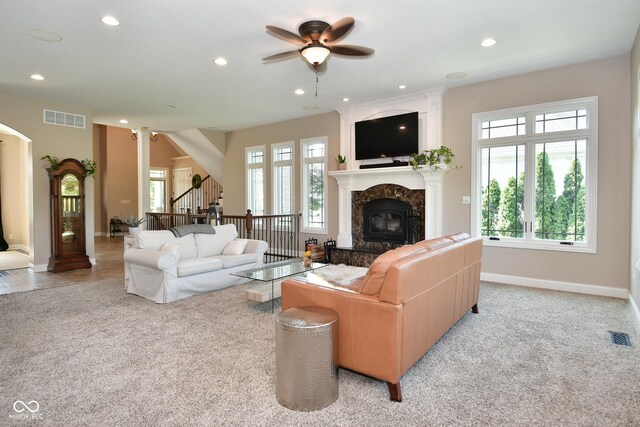 carpeted living room featuring a high end fireplace, plenty of natural light, and ceiling fan