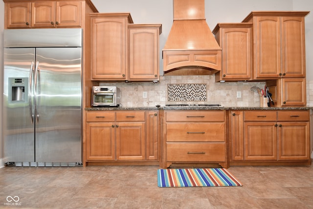 kitchen with dark stone counters, stainless steel appliances, custom exhaust hood, and light tile patterned floors