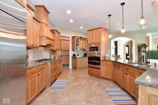 kitchen featuring visible vents, decorative backsplash, a sink, built in appliances, and dark stone counters