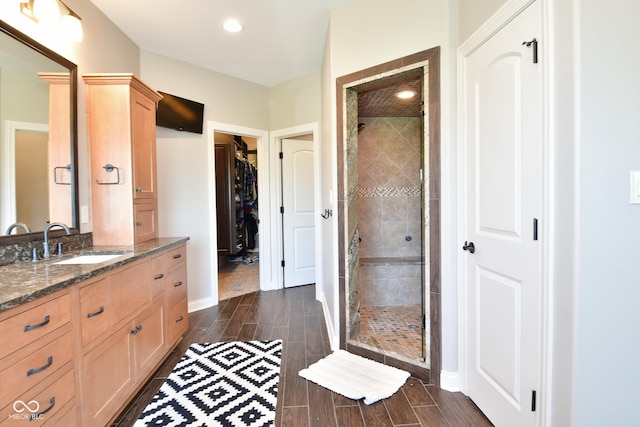 full bath with baseboards, a spacious closet, vanity, a shower stall, and wood finish floors