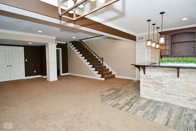 interior space featuring hanging light fixtures, crown molding, a breakfast bar area, ornate columns, and carpet