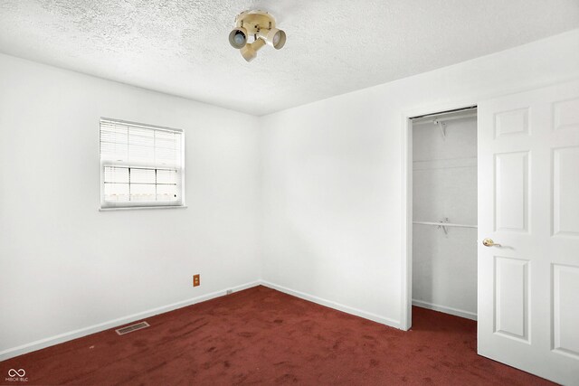 unfurnished bedroom with a closet, a textured ceiling, and dark carpet