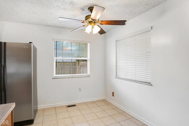 interior space with light tile patterned flooring, a textured ceiling, stainless steel refrigerator, and ceiling fan