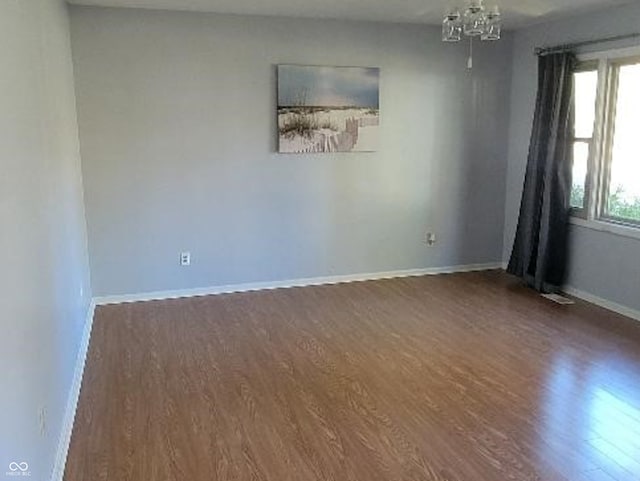 empty room featuring dark wood-type flooring and a notable chandelier