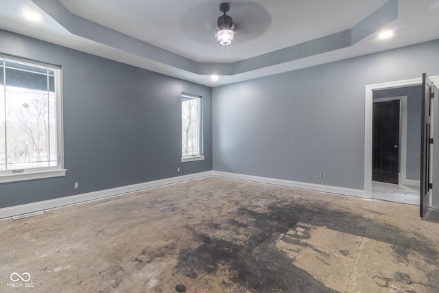 unfurnished room featuring ceiling fan, a healthy amount of sunlight, and a tray ceiling