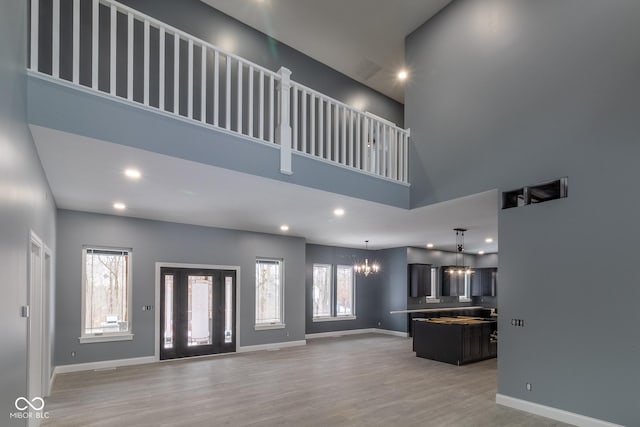 unfurnished living room featuring an inviting chandelier, a towering ceiling, and hardwood / wood-style flooring