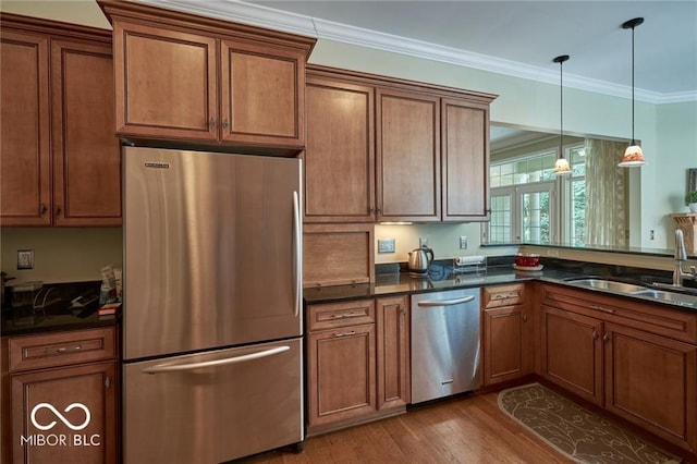 kitchen featuring sink, light wood-type flooring, ornamental molding, pendant lighting, and stainless steel appliances