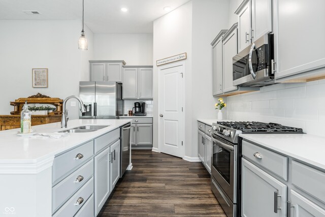 kitchen with a kitchen island with sink, dark wood-type flooring, stainless steel appliances, sink, and hanging light fixtures