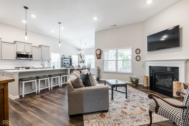 living room featuring a healthy amount of sunlight, vaulted ceiling, dark hardwood / wood-style floors, and a notable chandelier