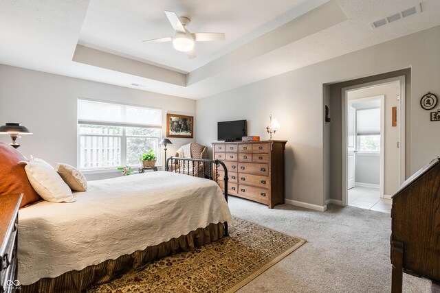 carpeted bedroom featuring a tray ceiling, connected bathroom, and ceiling fan