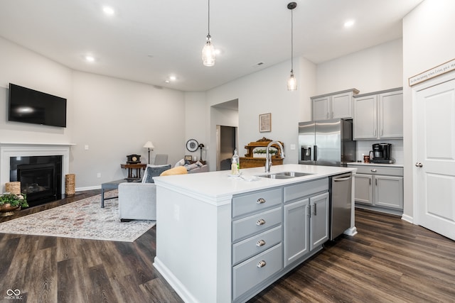 kitchen with appliances with stainless steel finishes, an island with sink, sink, and dark wood-type flooring