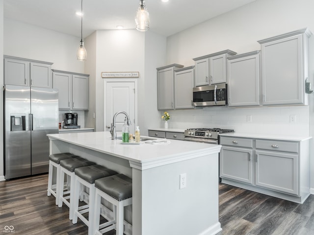 kitchen with appliances with stainless steel finishes, an island with sink, dark wood-type flooring, hanging light fixtures, and a kitchen bar