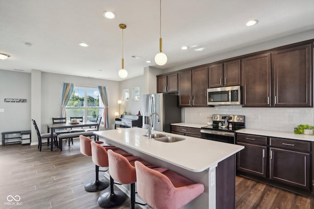 kitchen featuring pendant lighting, stainless steel appliances, sink, a center island with sink, and dark brown cabinets