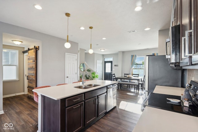 kitchen with a barn door, a center island with sink, appliances with stainless steel finishes, decorative light fixtures, and sink