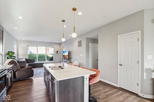 kitchen featuring decorative light fixtures, a center island with sink, sink, stainless steel appliances, and dark hardwood / wood-style flooring