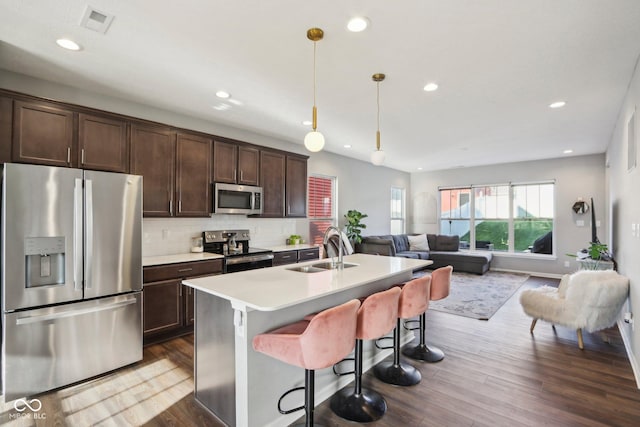 kitchen with a center island with sink, pendant lighting, sink, stainless steel appliances, and dark brown cabinets