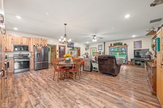 kitchen with light brown cabinetry, appliances with stainless steel finishes, ceiling fan with notable chandelier, and wood-type flooring