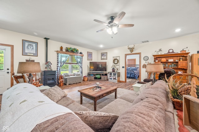 living room with a wood stove, light wood-type flooring, and ceiling fan