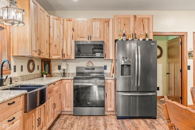 kitchen with appliances with stainless steel finishes, light hardwood / wood-style flooring, light brown cabinets, light stone countertops, and a chandelier