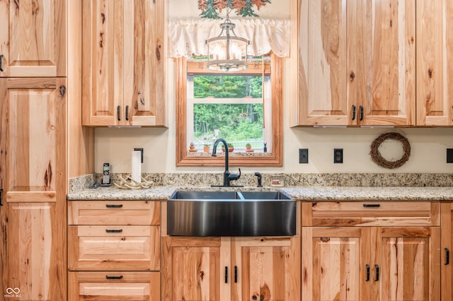 kitchen with sink, an inviting chandelier, light stone countertops, and light brown cabinets