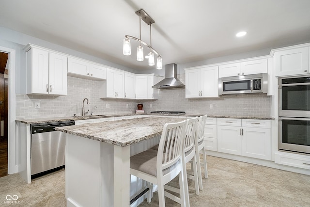 kitchen featuring light stone counters, stainless steel appliances, wall chimney range hood, white cabinetry, and a sink