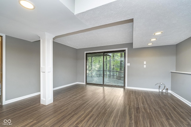 unfurnished living room with decorative columns, a textured ceiling, baseboards, and wood finished floors