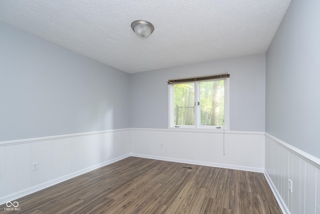 spare room with a wainscoted wall, dark wood-style flooring, a textured ceiling, and visible vents