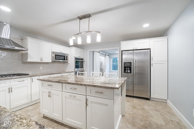 kitchen featuring a barn door, stainless steel appliances, white cabinets, wall chimney range hood, and backsplash