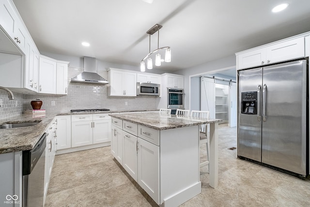 kitchen with a barn door, wall chimney exhaust hood, a sink, stainless steel appliances, and backsplash