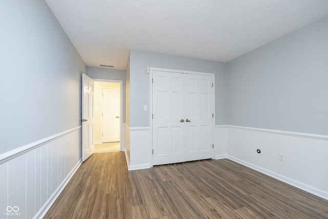 unfurnished bedroom with visible vents, a wainscoted wall, wood finished floors, a textured ceiling, and a closet