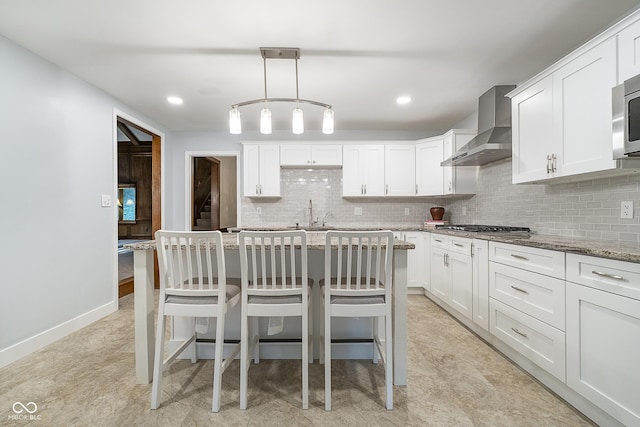 kitchen featuring stainless steel gas cooktop, tasteful backsplash, white cabinets, light stone countertops, and wall chimney exhaust hood