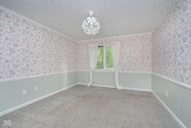 carpeted empty room with wallpapered walls, a textured ceiling, and a wainscoted wall