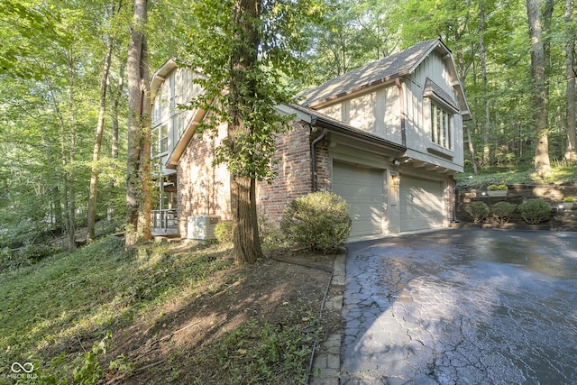 view of side of property featuring a garage, aphalt driveway, cooling unit, and brick siding