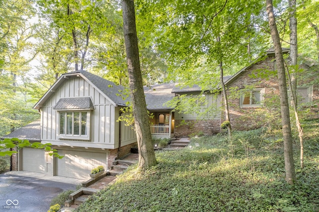 view of front of property featuring a shingled roof, aphalt driveway, an attached garage, board and batten siding, and brick siding