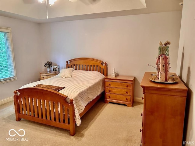 bedroom featuring light carpet, a tray ceiling, and ceiling fan