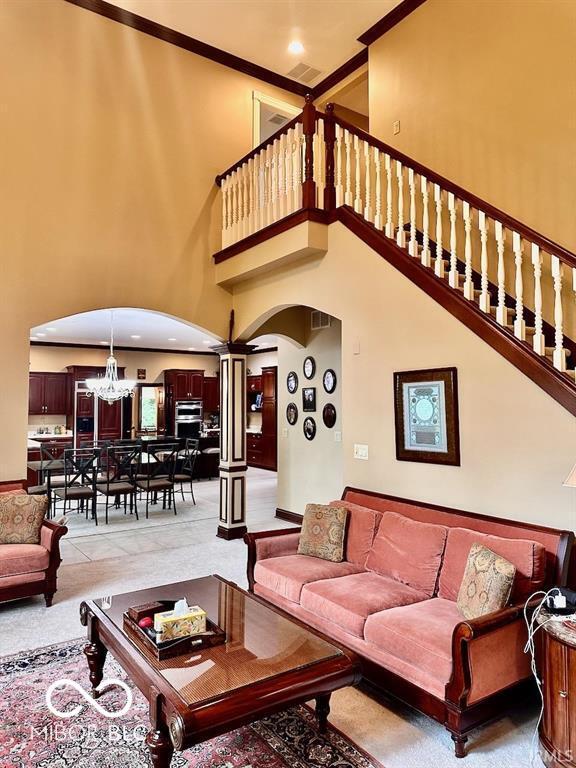 carpeted living room with an inviting chandelier, crown molding, and a high ceiling