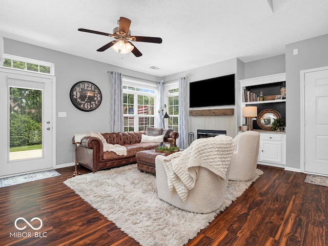 living room featuring built in features, a tiled fireplace, dark hardwood / wood-style flooring, and ceiling fan