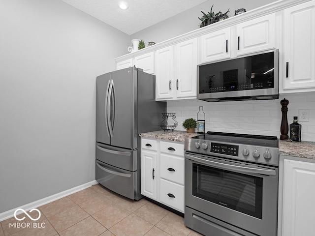 kitchen with light tile patterned flooring, white cabinetry, light stone counters, stainless steel appliances, and decorative backsplash