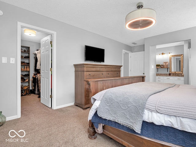 carpeted bedroom featuring a spacious closet, ensuite bath, and a textured ceiling