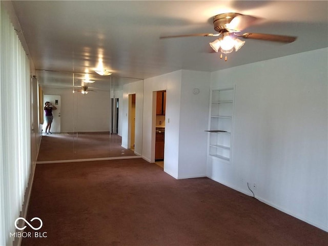 empty room featuring dark carpet, built in features, and ceiling fan