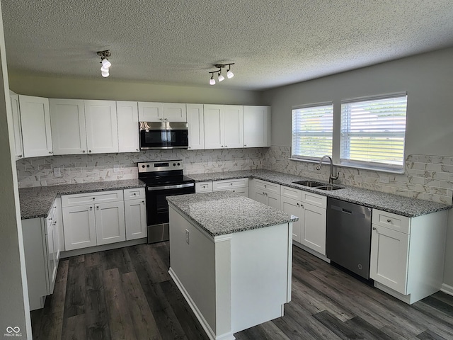 kitchen with sink, stainless steel appliances, light stone countertops, white cabinets, and a kitchen island