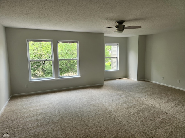 carpeted empty room featuring ceiling fan, a wealth of natural light, and a textured ceiling