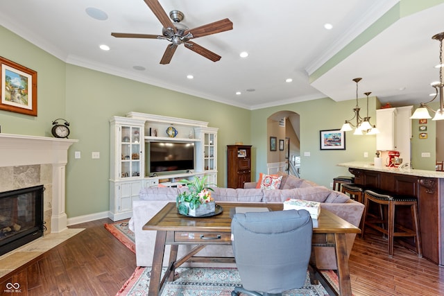 living room featuring dark wood-type flooring, ceiling fan, ornamental molding, and a tiled fireplace