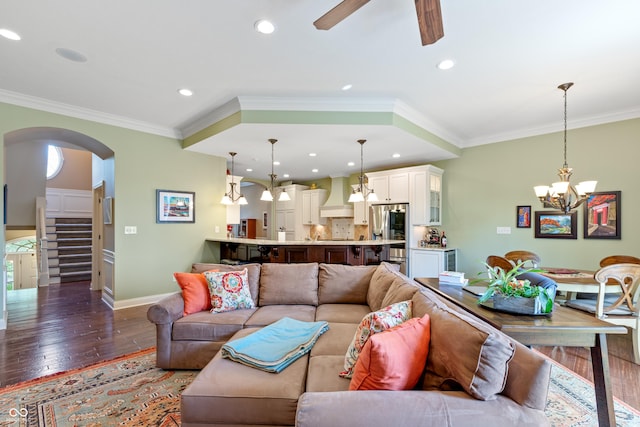 living room with ornamental molding, dark hardwood / wood-style flooring, and ceiling fan with notable chandelier